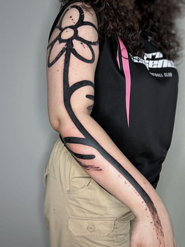 A woman showing off her arm with a vibrant flower tattoo, highlighting her unique style and personality.