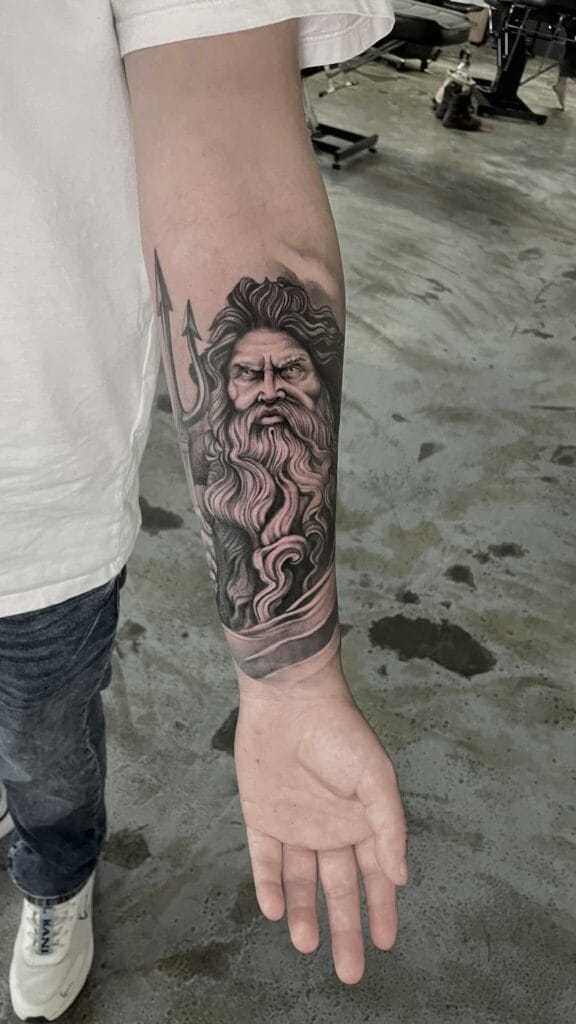 A man shows off his arm tattoo of a bearded figure, inspired by Poseidon, showcasing intricate details and artistry.